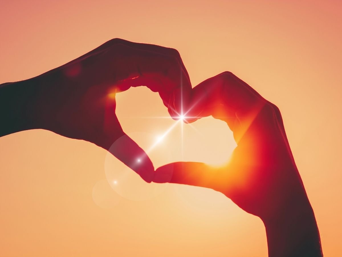 Two hands forming a heart, back-lit by a warm Sun, representing love