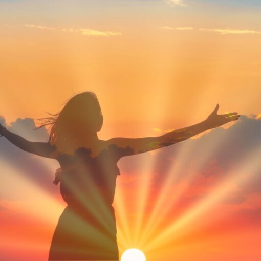 Individual standing in the sunrise with arms lifted toward the sun during summer solstice ritual.