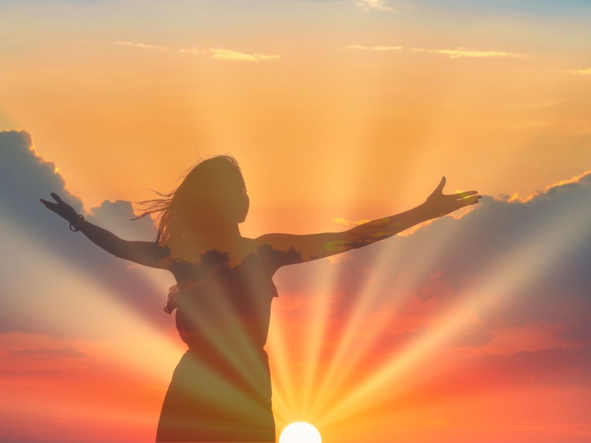 Individual standing in the sunrise with arms lifted toward the sun during summer solstice ritual.