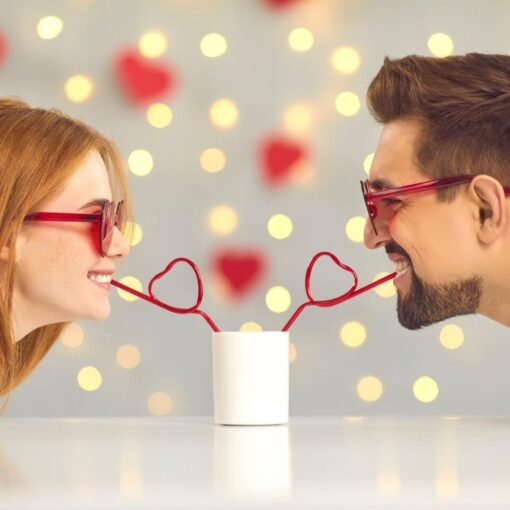 A woman and a man share a drink using heart-shaped straws