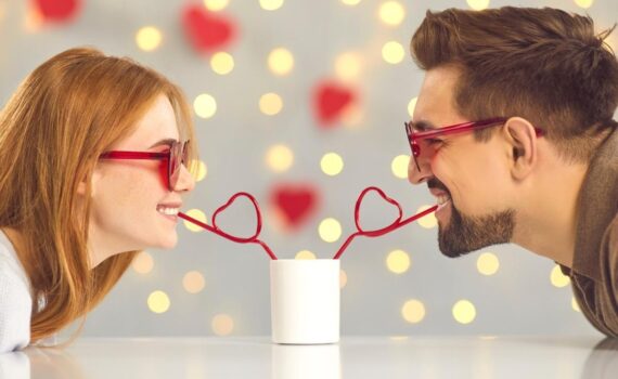 A woman and a man share a drink using heart-shaped straws