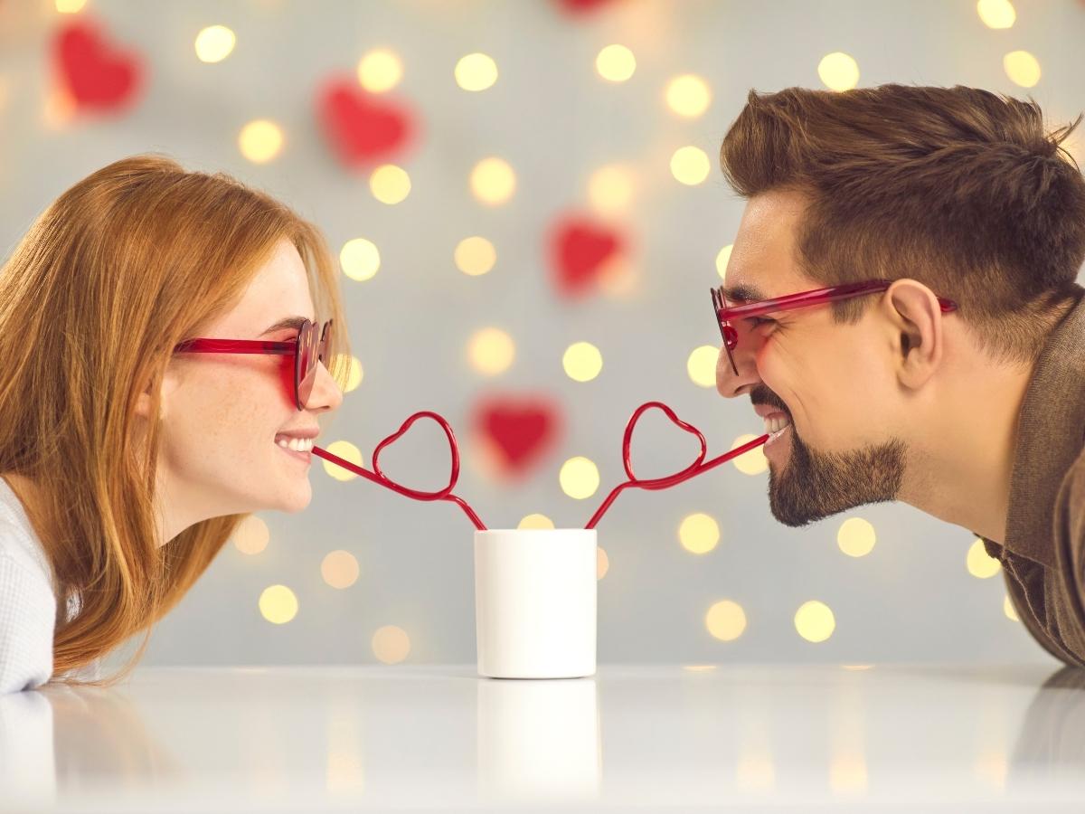 A woman and a man share a drink using heart-shaped straws